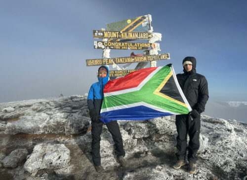 Two climbers holding a South African flag at the summit of Mt. Kilimanjaro