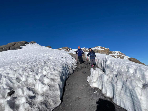 2 people descending from the summit of Mount Kilimanjaro on a path carved out in the snow.
